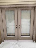 Exterior double doors with glass panes installed, showing front view with snow on the ground.