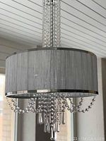 Ceiling light fixture with grey cylindrical fabric shade and multiple clear crystal bead strands hanging below and around the shade.