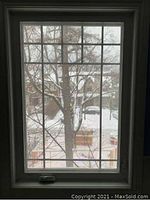 Front view of white framed casement window with grid muntins and crank handle at bottom, set within trim.