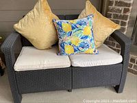 Loveseat shows dark grey synthetic wicker frame with two white seat cushions and three decorative pillows (gold and lemon pattern).