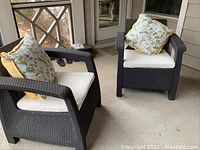 Photo showing two matching dark brown faux wicker outdoor chairs with white cushions and floral pillows on a porch.