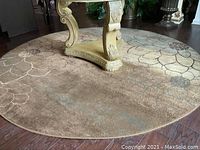 Full view of the round beige rug with floral pattern under a table base, showing the wear and need for cleaning.