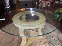 Angled top view of round glass table showing beveled edges and carved wooden base structure beneath.