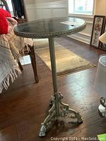 Full side view showing the round tabletop and three-legged cast iron base with claw feet and intricate details.