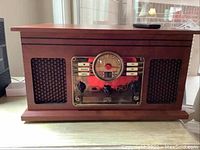 Full view of wooden radio with central analog dial, speakers on either side with woven grille, and metal control panel with buttons and knobs.