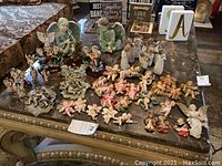 Wide view of over 40 angel figurines of varying sizes and styles displayed on a marble table.