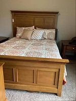 Full view of maple queen bed with assembled headboard and footboard, complete with decorative linens and pillows.