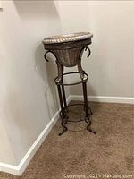 Full view of tall resin bowl plant stand with metal legs and glass insert on top.