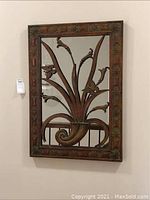 Full view of the decorative metal wall art mirror hung on wall showing detailed frame and metal floral design within mirror body.