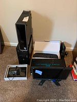 Several computer components including two desktop computers, multiple keyboards, a Mechanical Eagle monitor, and cables on carpeted floor against beige wall.