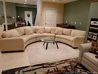 Full view of the large ivory semi-circle sectional sofa in a living room, showing its curved shape and multiple matching throw pillows.