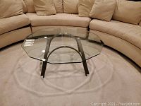Full view of the coffee table showing the 12-sided beveled glass top and metal base in front of a beige curved sofa.