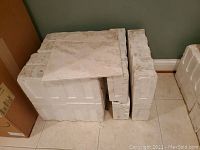 Stack of off white terrazzo tiles in protective foam packaging against a green wall.