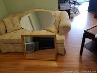 Photo showing both the oval beveled mirror and the rectangular framed mirror placed on a beige floral couch and floor.