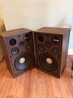 Pair of Lyric Model F42 loudspeakers shown side by side on floor with wooden cabinets and multiple drivers exposed