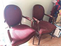Two vintage ship armchairs with oval backs and red upholstery, showing signs of wear and damage.