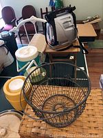 Photo of picnic basket, metal wire basket, thermos jugs, and TV lantern arranged on a wooden table.
