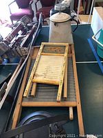 Wide shot of all items laid out on table showing three washboards, white cast iron kettle, metal pitcher, and vintage thermos, capturing overall condition and content of the lot.