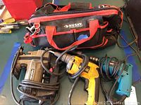 Photo showing Dewalt corded drill, Chicago electric drill, porter cable saw, and Husky tool bag