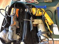 Photo showing the Dewalt electric drill in yellow with black branding along with the Sears Sabre saw and Ridgid multi-tool on a table with cords visible, showing cosplay cases and wear on tools.