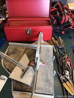 Full view of red metal toolbox, Superior tile cutter, and assorted hand tools including screwdrivers and pliers on a tabletop.