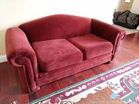 Front view of red upholstered loveseat sofa on wood floor near patterned rug