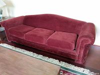 Red upholstered sofa from a front angle showing three seat cushions and rolled arms on a wooden floor with rug in front.
