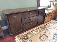 Front view of a rectangular wood credenza with three central drawers and two cabinet doors on the sides. Brass handles on drawers and doors. Visible scratches and stains on the wood surface.