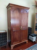 Front view of Stickley wood armoire with double doors closed, showing brass handles and arched panel design