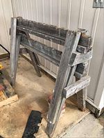Pair of weathered wooden sawhorses with clear view of one sawhorse showing its side and leg structure.