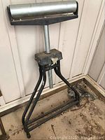 Full view of woodworking roller stand showing metal roller, vertical adjustable shaft, and black metal base frame on floor against wall