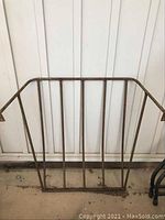 Front view of metal wall mount hay cage showing rectangular structure and vertical bars with rust spots.