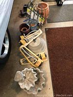 Photo showing two-tier stone-look fountain, yellow rotary sprinkler, terracotta pots, metal umbrella stand, metal fencing section, and bucket.