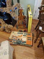 Photo showing All Metal Service Station toy box, crochet set with hooks in metal stand, rubber horseshoe game, yellow folding table, partially visible furniture items