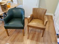 Pair of brown and green arm chairs on wooden floor near white wall and refrigerator.