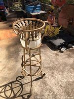 Full view of the gold iron planter stand with glass insert showing the classical leaf motifs and curled legs.