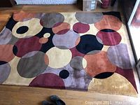 Full view of rectangular handmade area rug featuring overlapping circles in black, cinnamon, wine and neutral colors on wooden floor.
