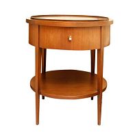 Front view of round wooden side table showing circular top, drawer, four legs and lower tiered shelf with light brown stain.