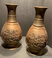 Front view of pair of brass Japanese vases showing applied floral motif.