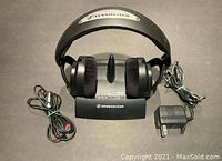 Front view showing Sennheiser wireless headphones resting on the transmitter base with power adapter and connecting cables visible.