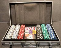Closed aluminum poker chip carrying case open displaying five stacks of poker chips in white, red, black, green, and blue with card decks and dealer chips in the center.
