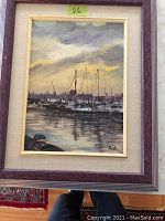 Framed oil painting of a harbor scene with boats under cloudy sky, signed by Joyce Allan, showing the purple wood frame with a small mark.