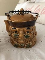 Front view of the Benjamin Franklin figurative ceramic teapot with distinctive features including wire handle, wooden knob on lid, facial details, and bow tie.