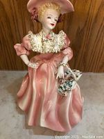 Front view of the 9-inch tall porcelain figurine showing detailed pink dress, lace collar, hat with ribbon, and a purse decorated with flowers.