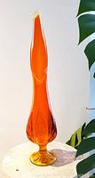 Side view of tall fire orange hand blown art glass vase showing elongated shape and round footed base.