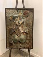 Close-up frontal view of metal relief artwork on easel