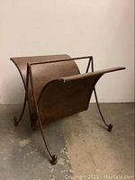 Front side view of the large metal magazine rack showing curved metal panels and ball feet on four legs.