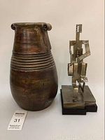 Photo showing front view of brown ceramic vase and metal abstract sculpture side by side.