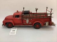 Side angle of the entire red decorative fire truck model showing ladder, hose reel, mounted lights, and detailed features.