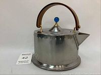 Full side view of vintage stainless steel teapot showing wood handle, blue lid knob, and riveted details.